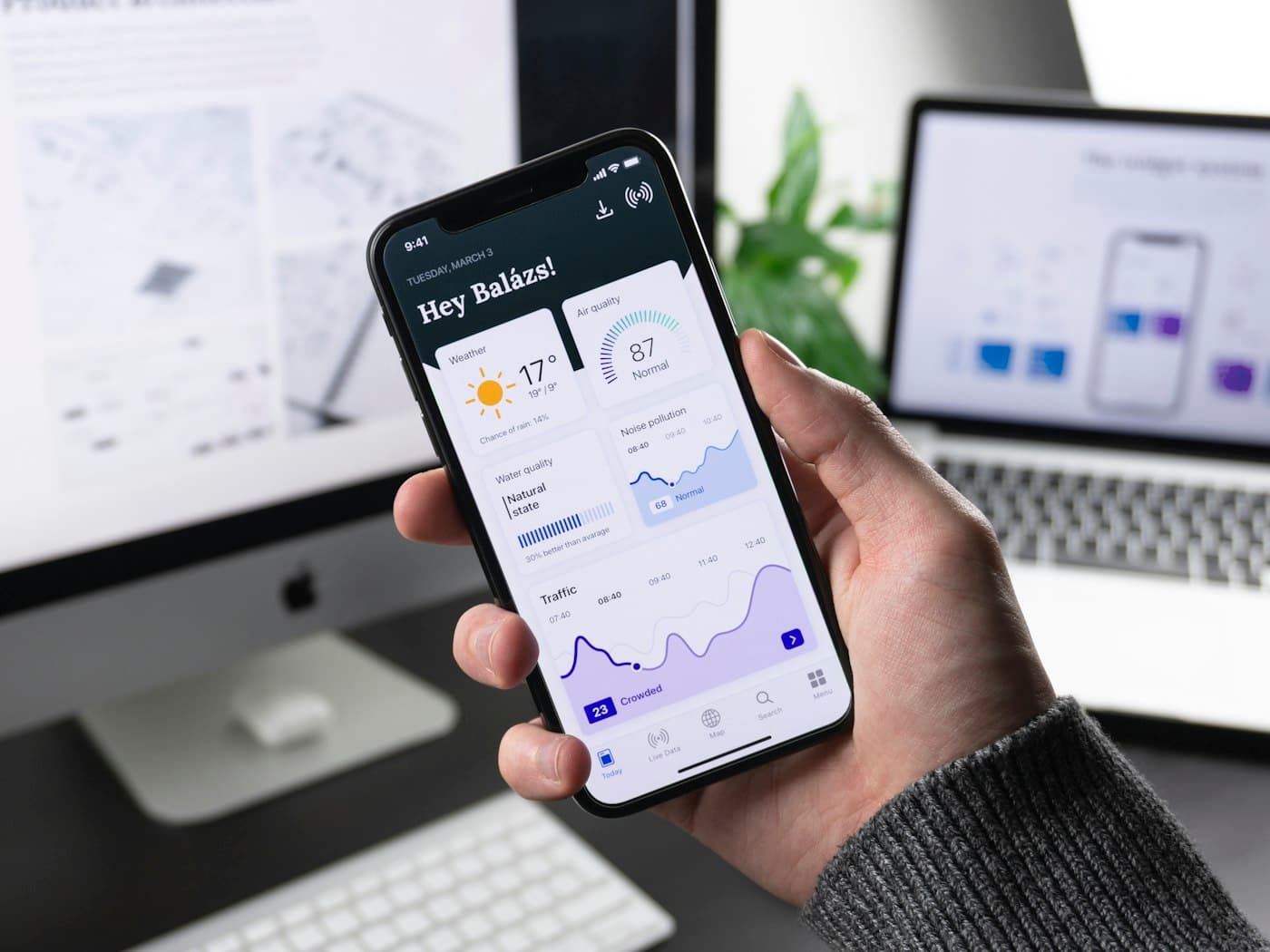 A hand holding a phone that shows a finished mobile app dashboard