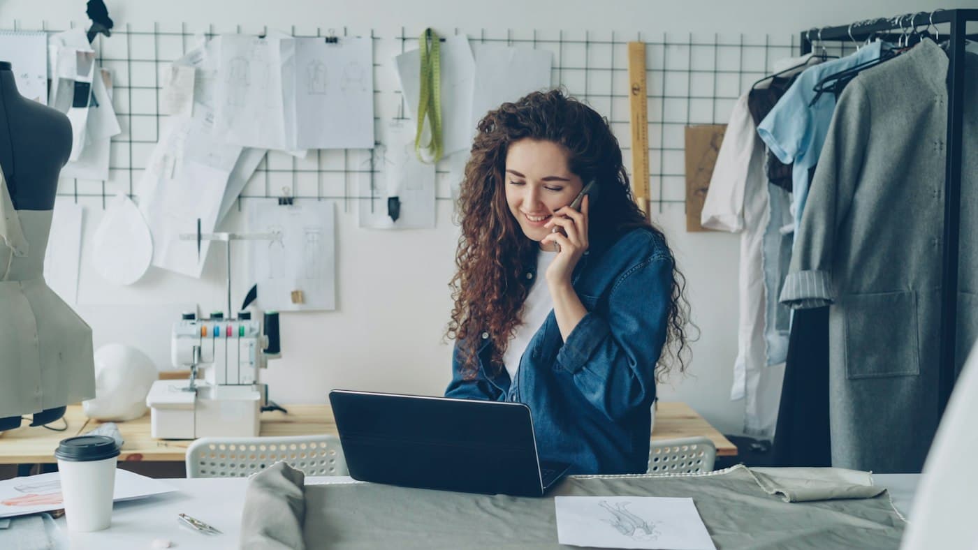 A small business owner on the phone at her workshop desk with a laptop open