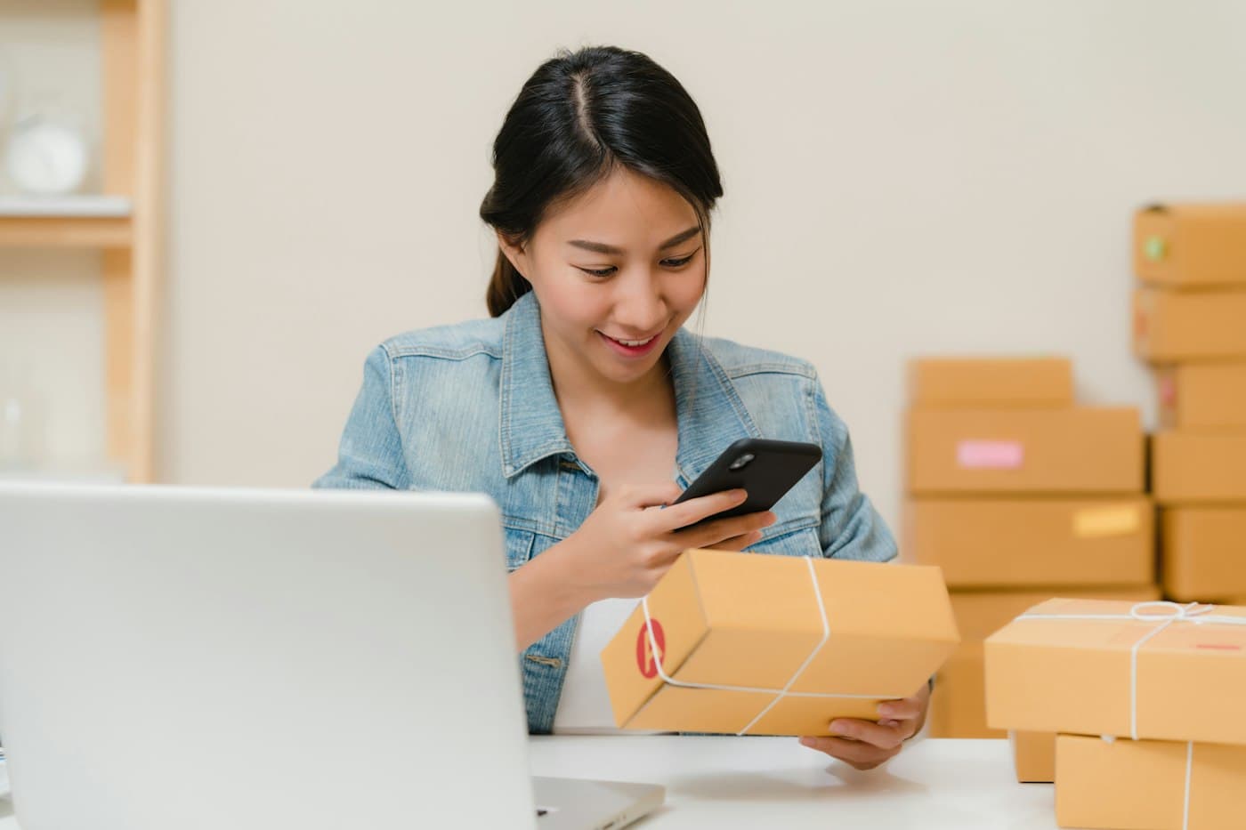 An online store owner packing a customer order and checking it on her phone